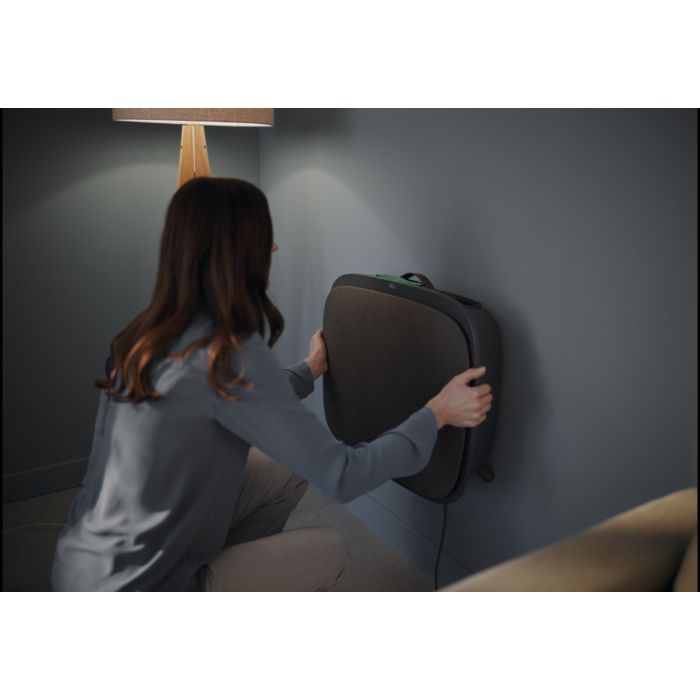 Una mujer monta un dispositivo rectangular oscuro en una pared gris cerca de una lámpara.