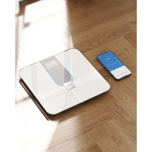 Una báscula inteligente blanca y un smartphone en suelo de madera.