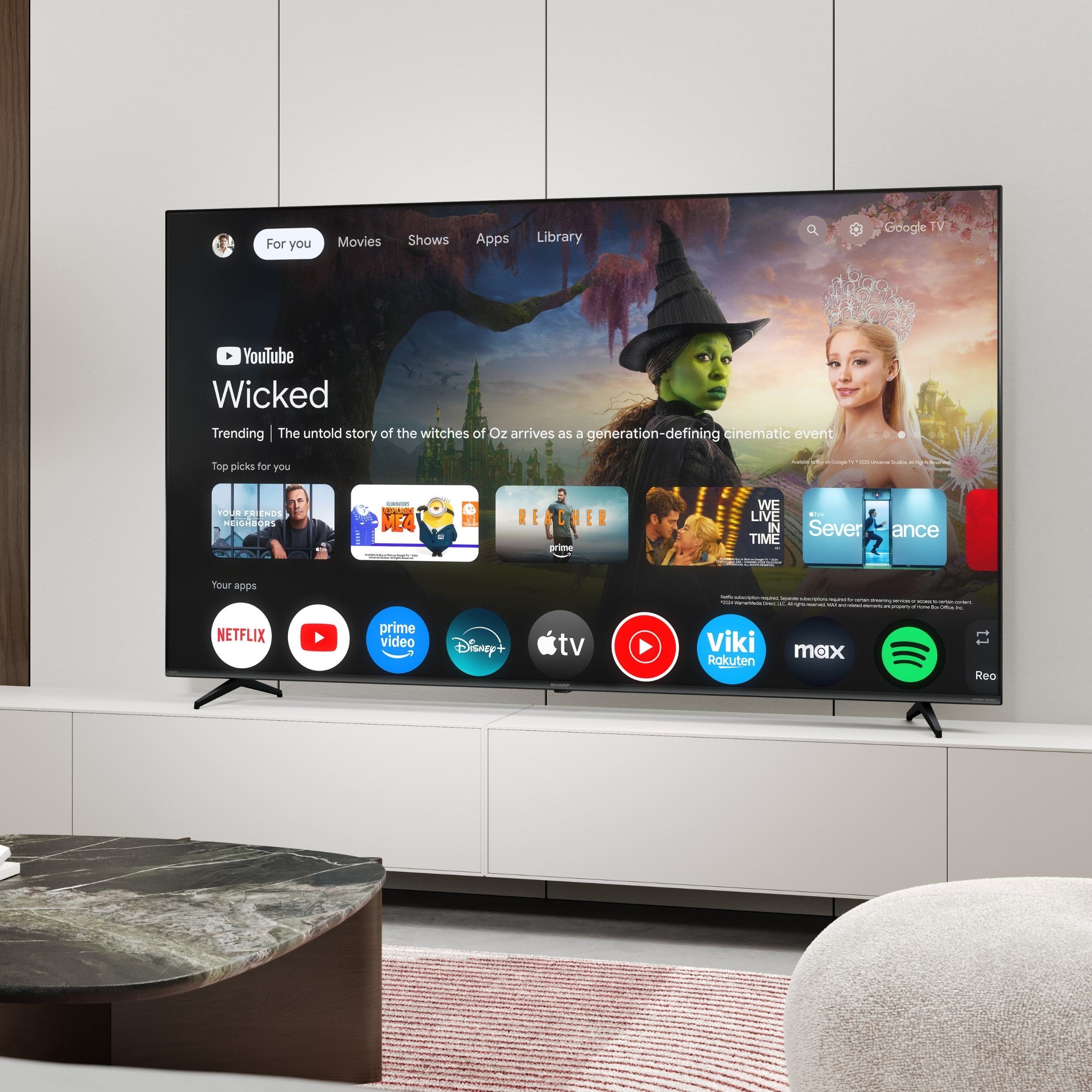 Ein moderner Fernseher zeigt die Google TV-Oberfläche mit 'Wicked'-Filmbildern und App-Symbolen.