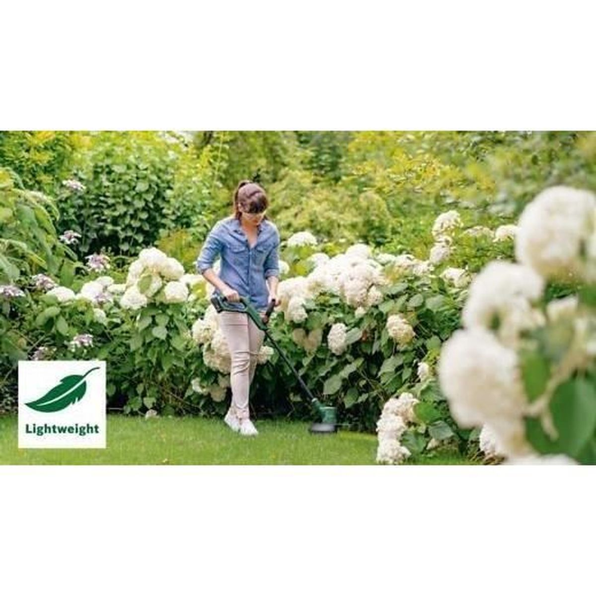 Frau trimmt Rasen zwischen Blumenbeeten mit einem Rasentrimmer.