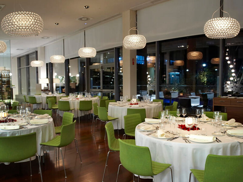 Un comedor formalmente puesto con mesas redondas, sillas verdes y luces colgantes modernas.