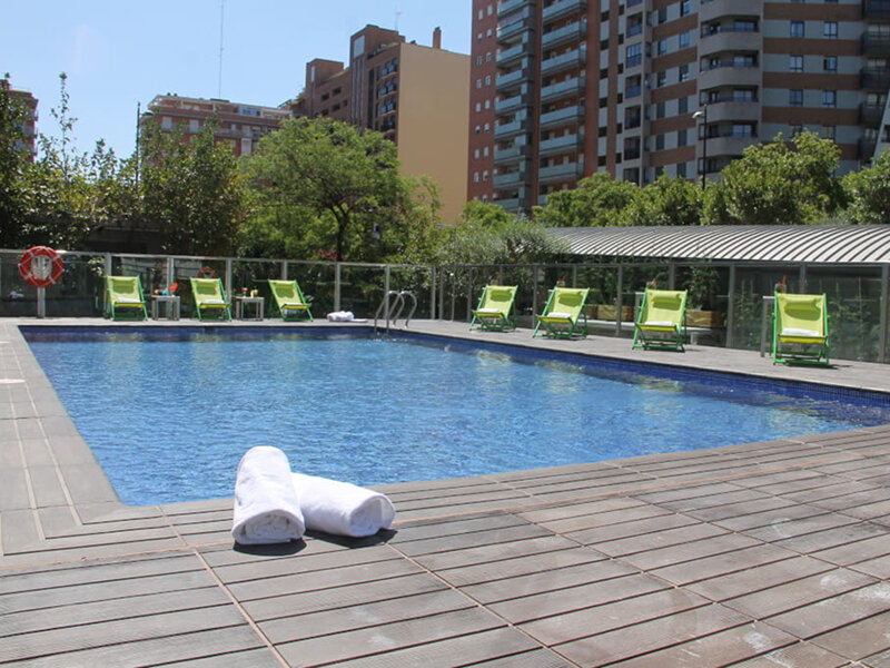 Una piscina con tumbonas y toallas en primer plano, edificios al fondo.