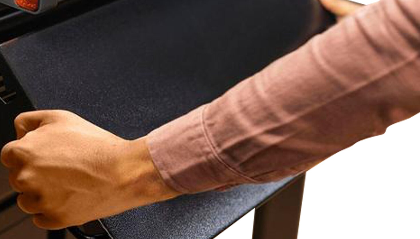 Una mano con camisa rosa sostiene un dispositivo electrónico negro.