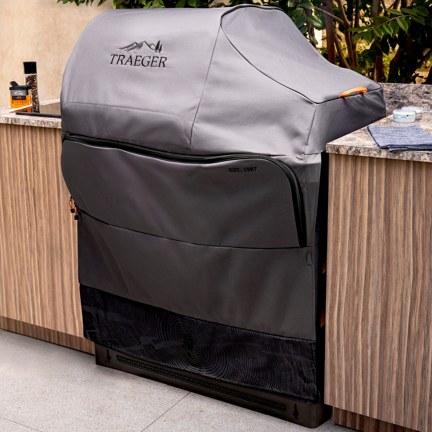 Funda gris para parrilla Traeger sobre encimera de piedra e isla de cocina.