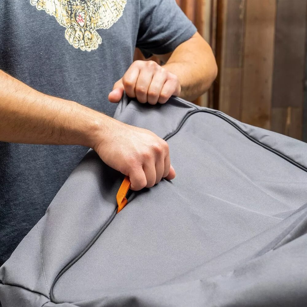 Manos agarran un lazo naranja en una cubierta gris con cremallera. Viste camisa gris.