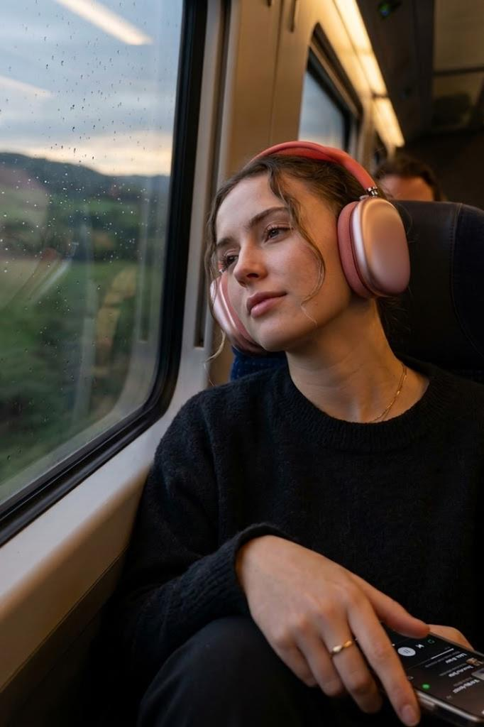 Kulaklıklı genç kadın yağmurlu günde tren penceresinden dışarı bakıyor.
