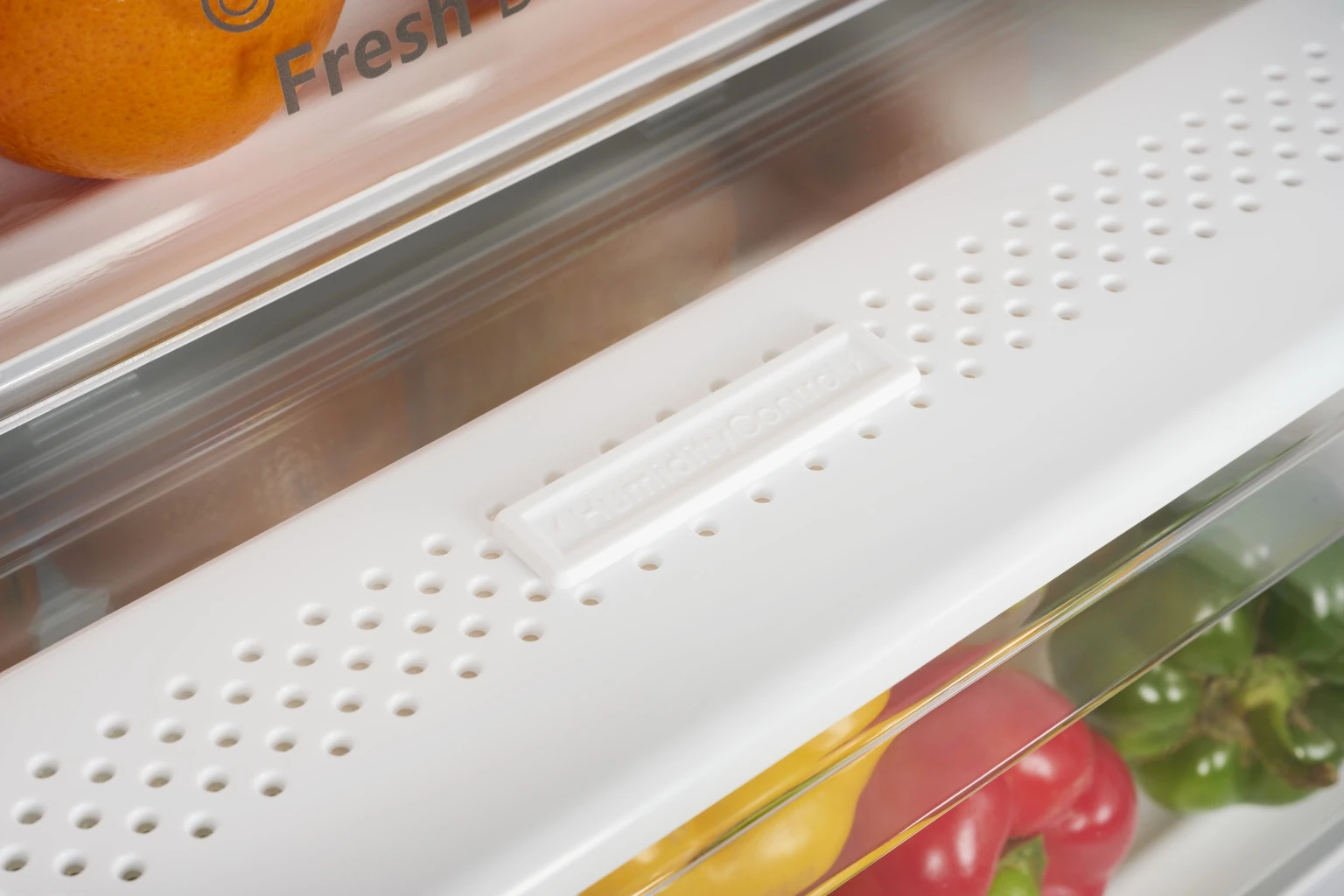 A close-up of an orange and peppers in a refrigerator drawer.