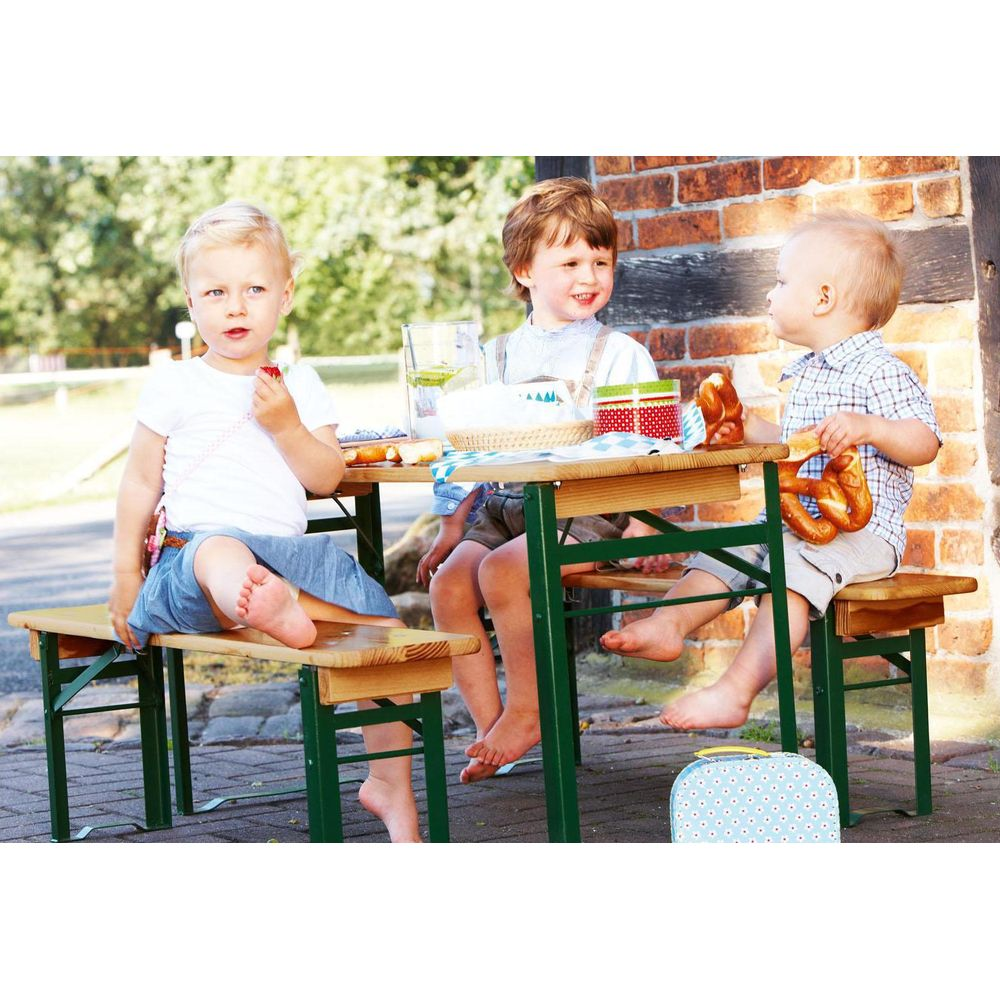 Drei kleine Kinder sitzen draußen an einem Holztisch und essen Brezeln und Obst.