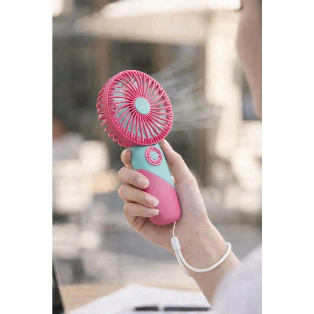 Bir el, hava üfleyen pembe ve turkuaz renkli taşınabilir bir fan tutuyor.