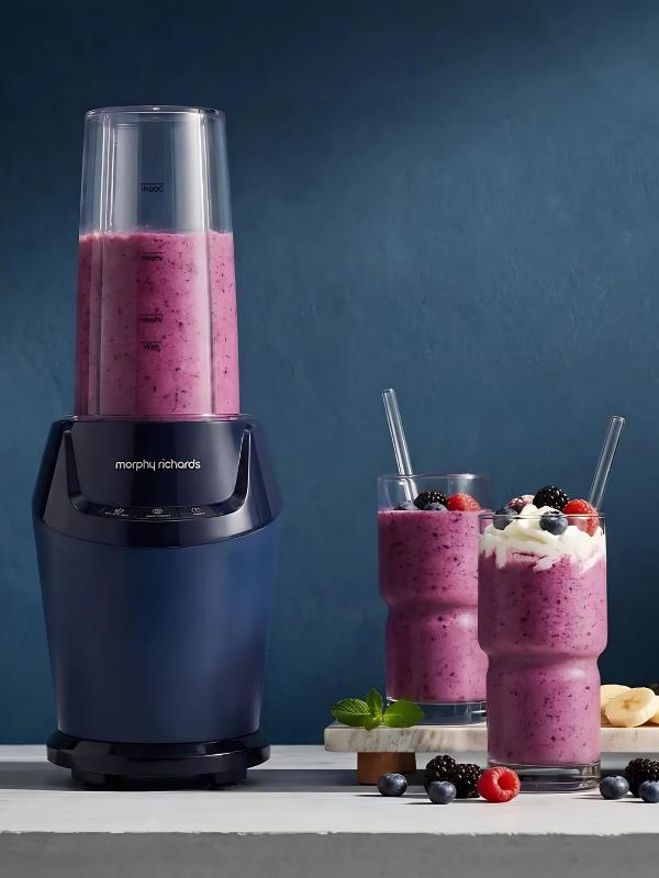 Üzeri süslenmiş iki böğürtlenli smoothie bardağının yanında mavi bir blender duruyor.