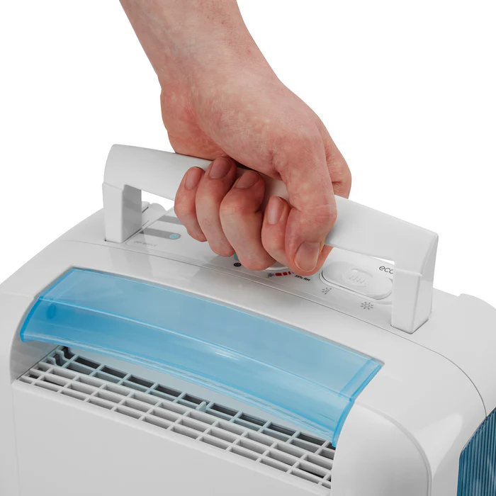 A hand grips the white handle of a white dehumidifier with a blue water tank.