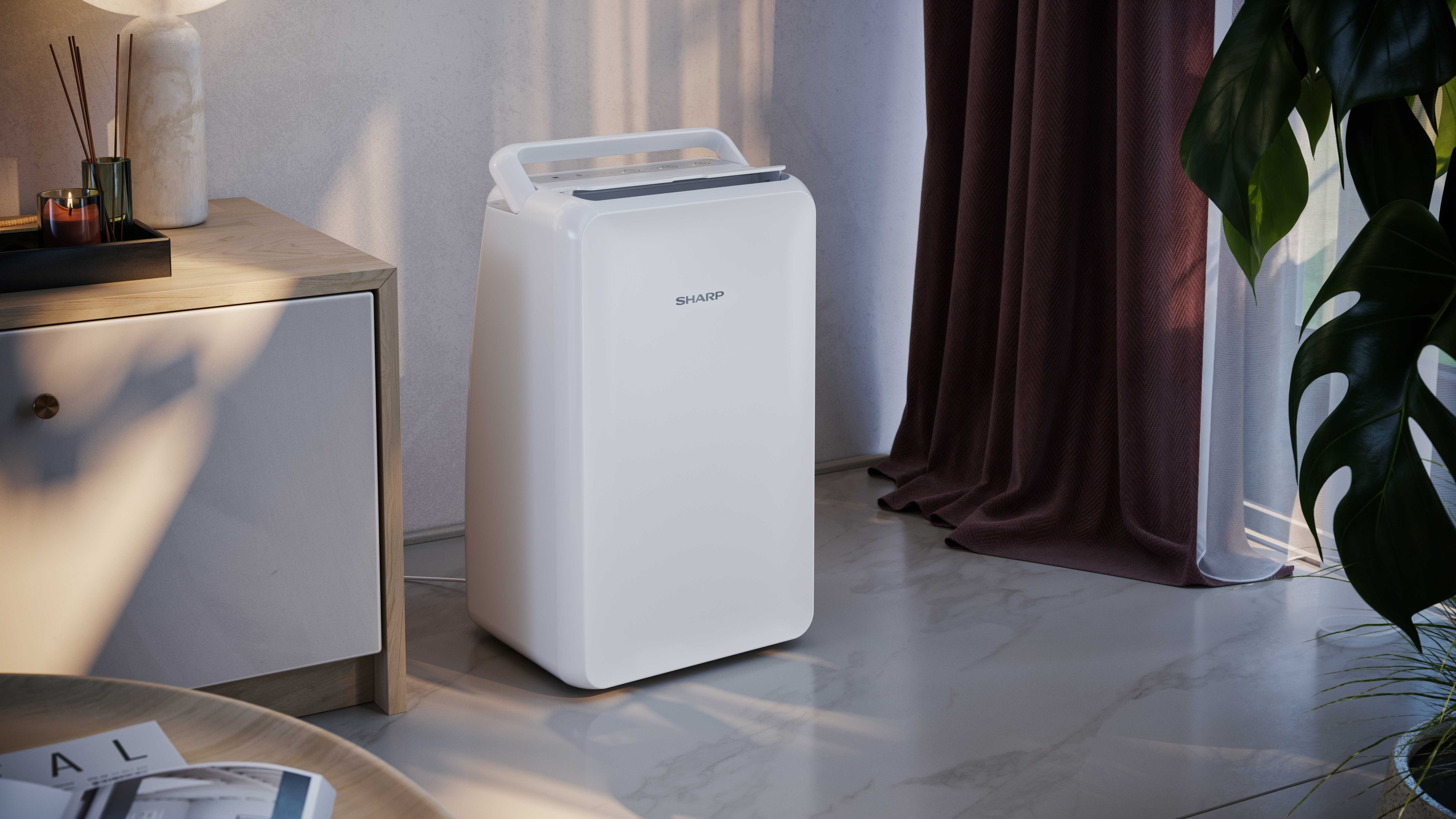 A white SHARP dehumidifier sits next to a nightstand. Dark curtains and plants are in the background.