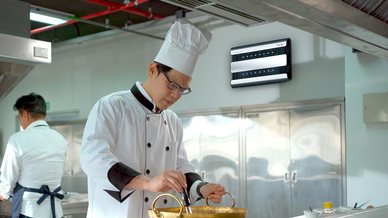 Chef in white uniform works in kitchen; devices on wall.