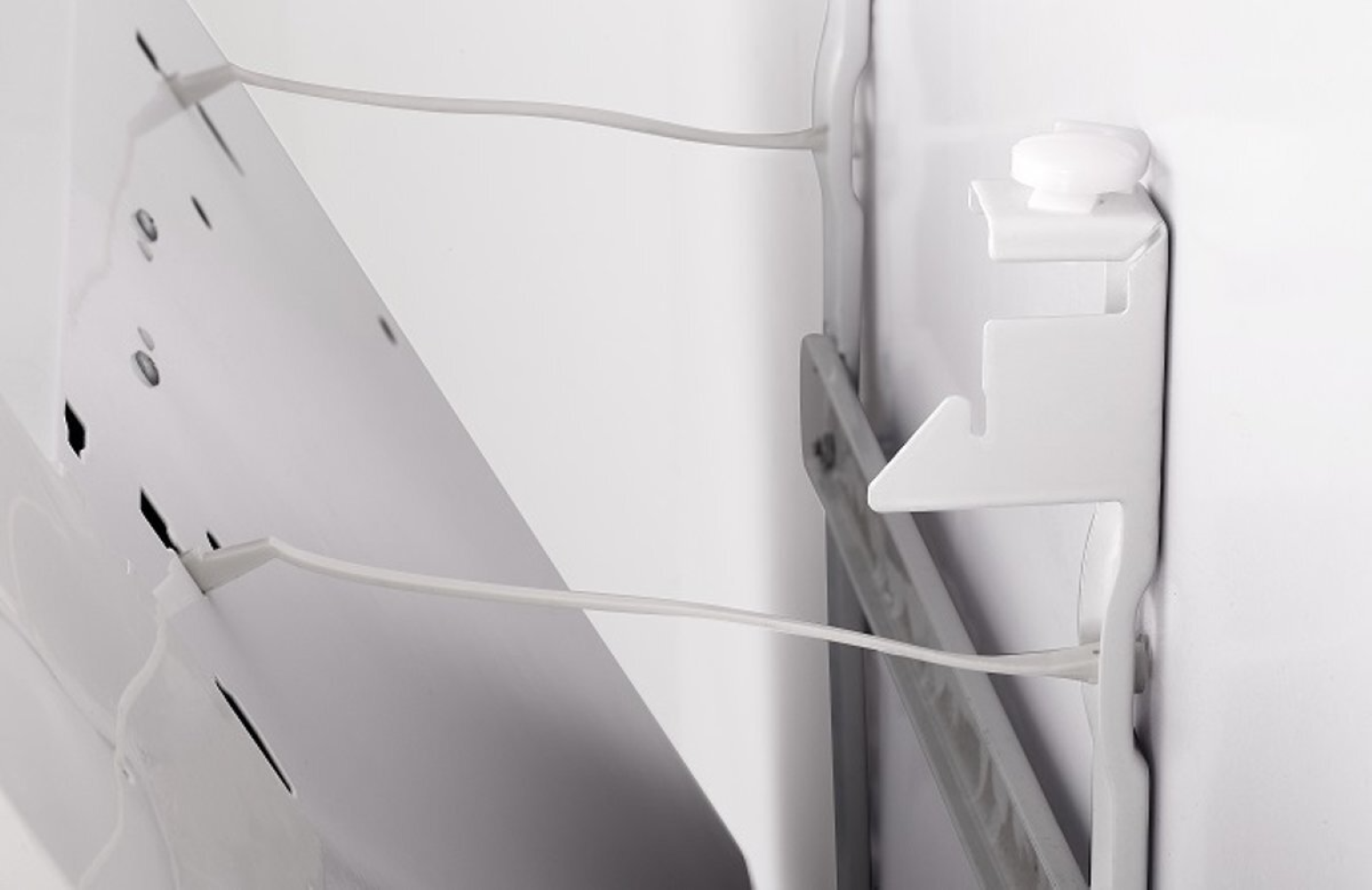 Close-up view of white plastic brackets holding a white surface, with thin wires attached.