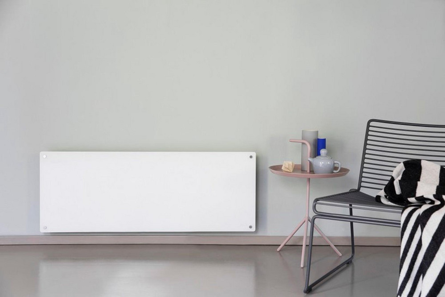 A white heater on a wall next to a small table with a teapot and a chair.