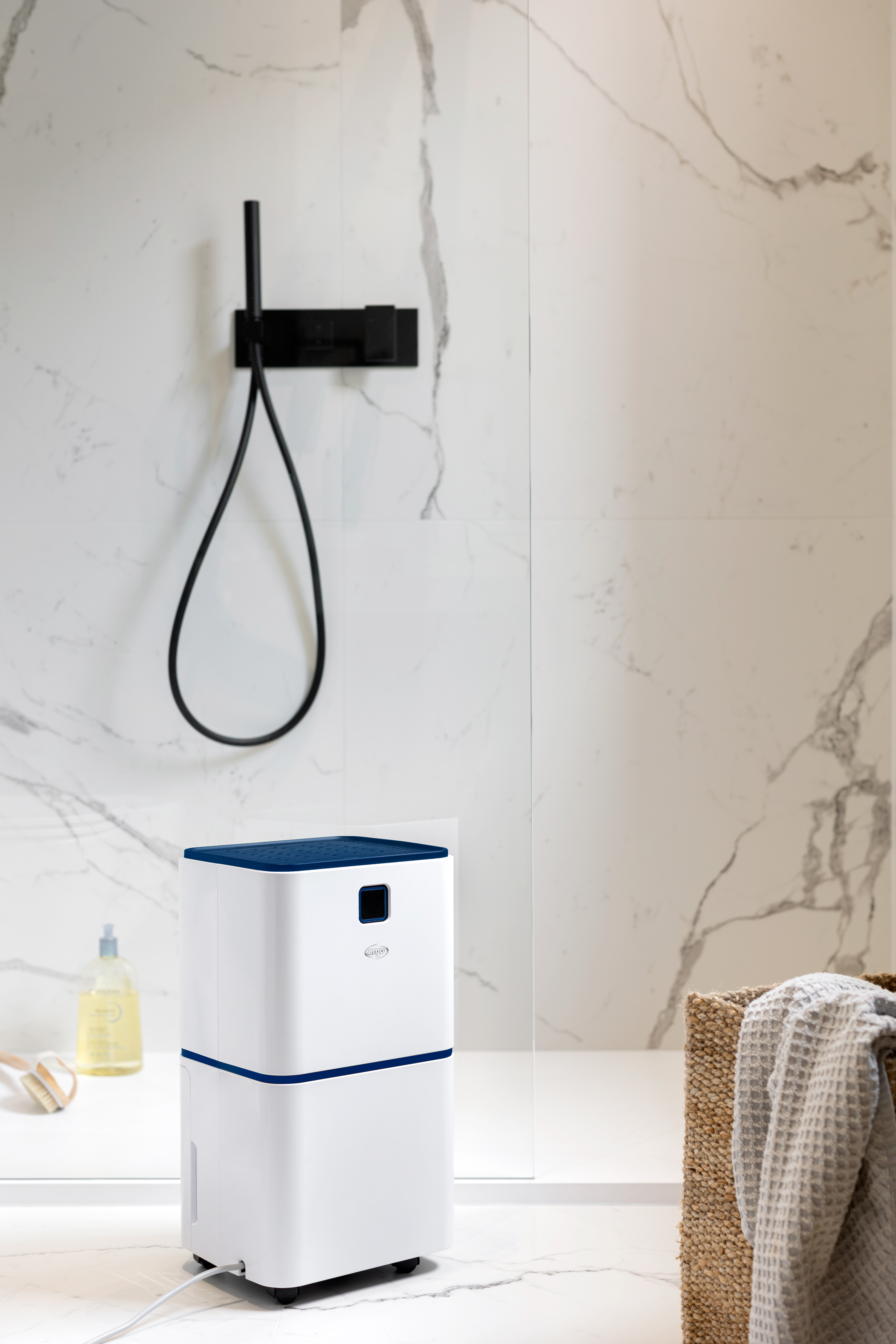 Un deshumidificador blanco con tapa azul está junto a una ducha, dispensador de jabón y cesta.