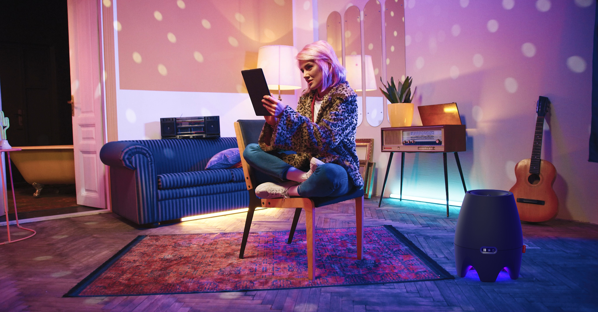 A woman with pink hair sits on a chair looking at a tablet.