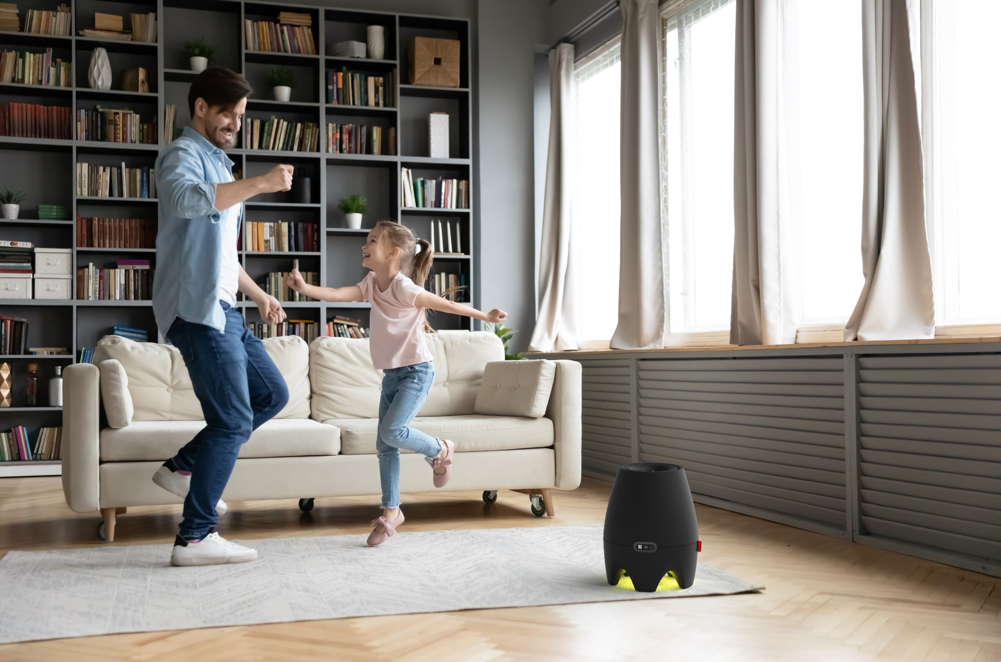 Father and daughter dancing in front of a sofa in a living room with bookshelves.