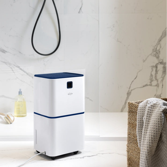 Un deshumidificador blanco con tapa azul está en un baño junto a una cesta.