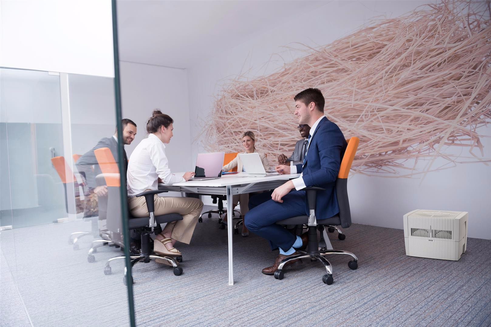 People in a meeting room with laptops and an air purifier in the foreground.