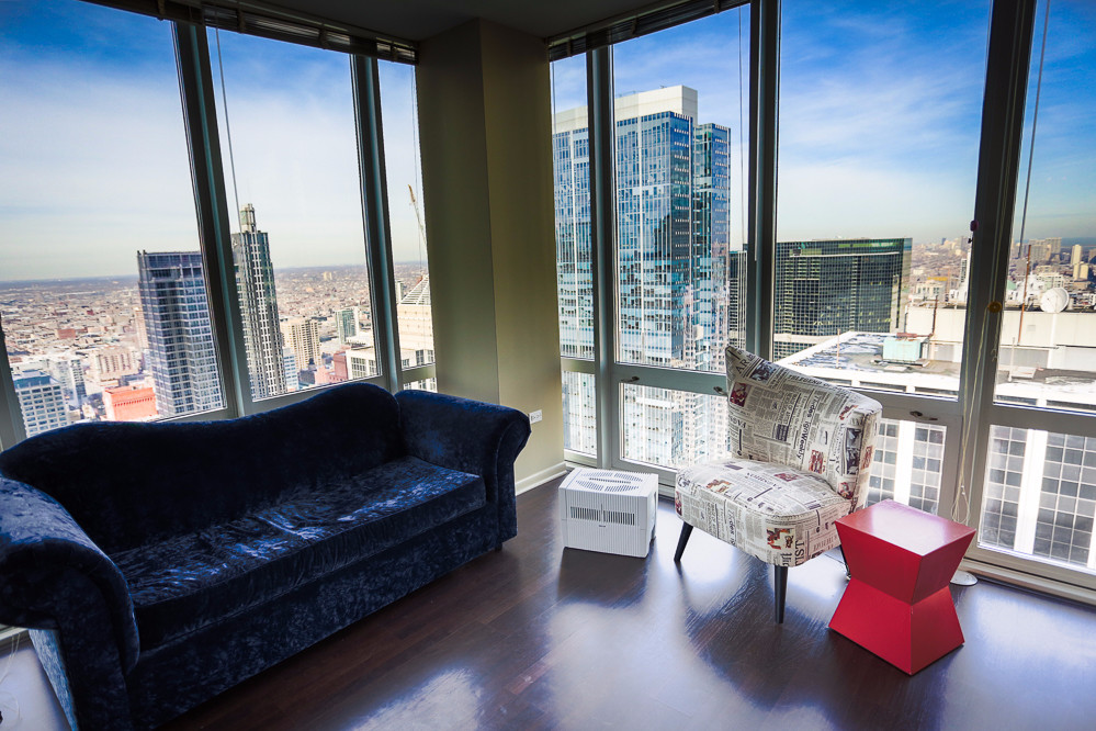 A dark sofa and newspaper-print armchair by windows with city view.