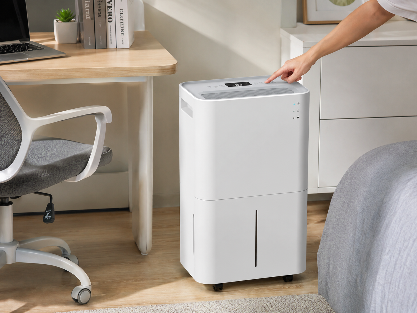 A person presses buttons on a white dehumidifier next to a desk with a laptop.