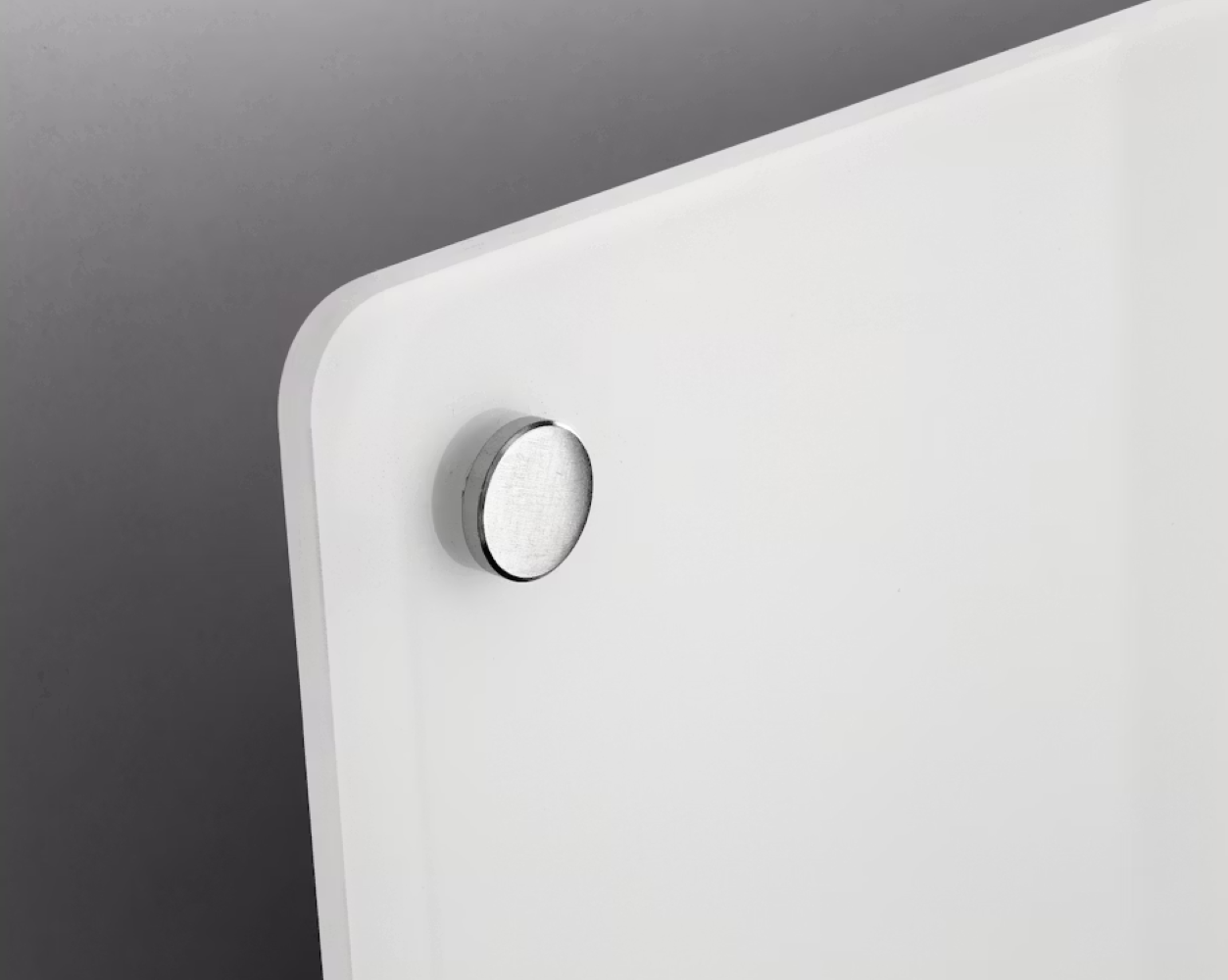 A silver magnet is attached to a white board hanging on a gray wall.