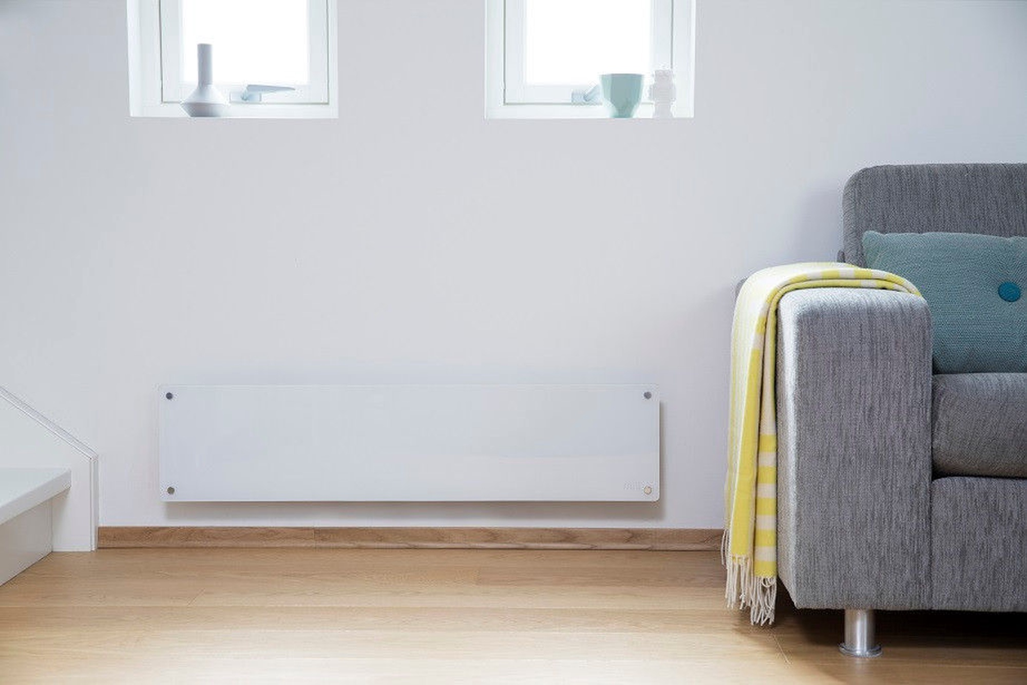A white wall heater is mounted on the wall next to a sofa with a yellow blanket.