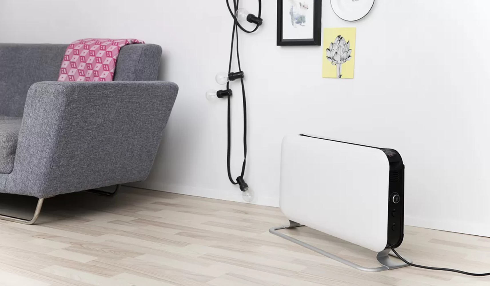 Un calentador blanco está sobre un suelo de madera junto a un sofá gris.