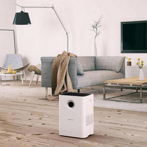 Ein weißer Luftreiniger steht auf einem Holzboden vor einem grauen Sofa.