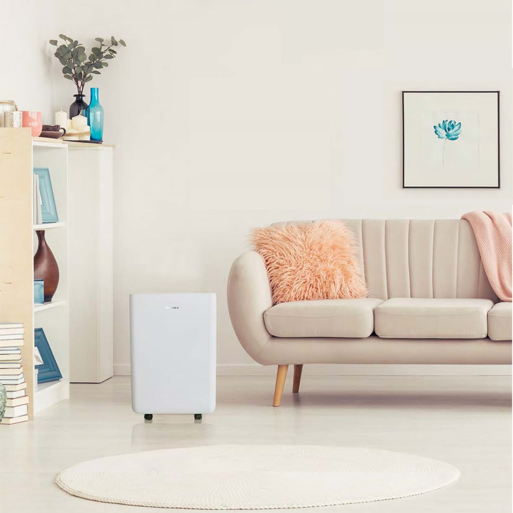 A white air purifier stands on a round rug in front of a sofa.