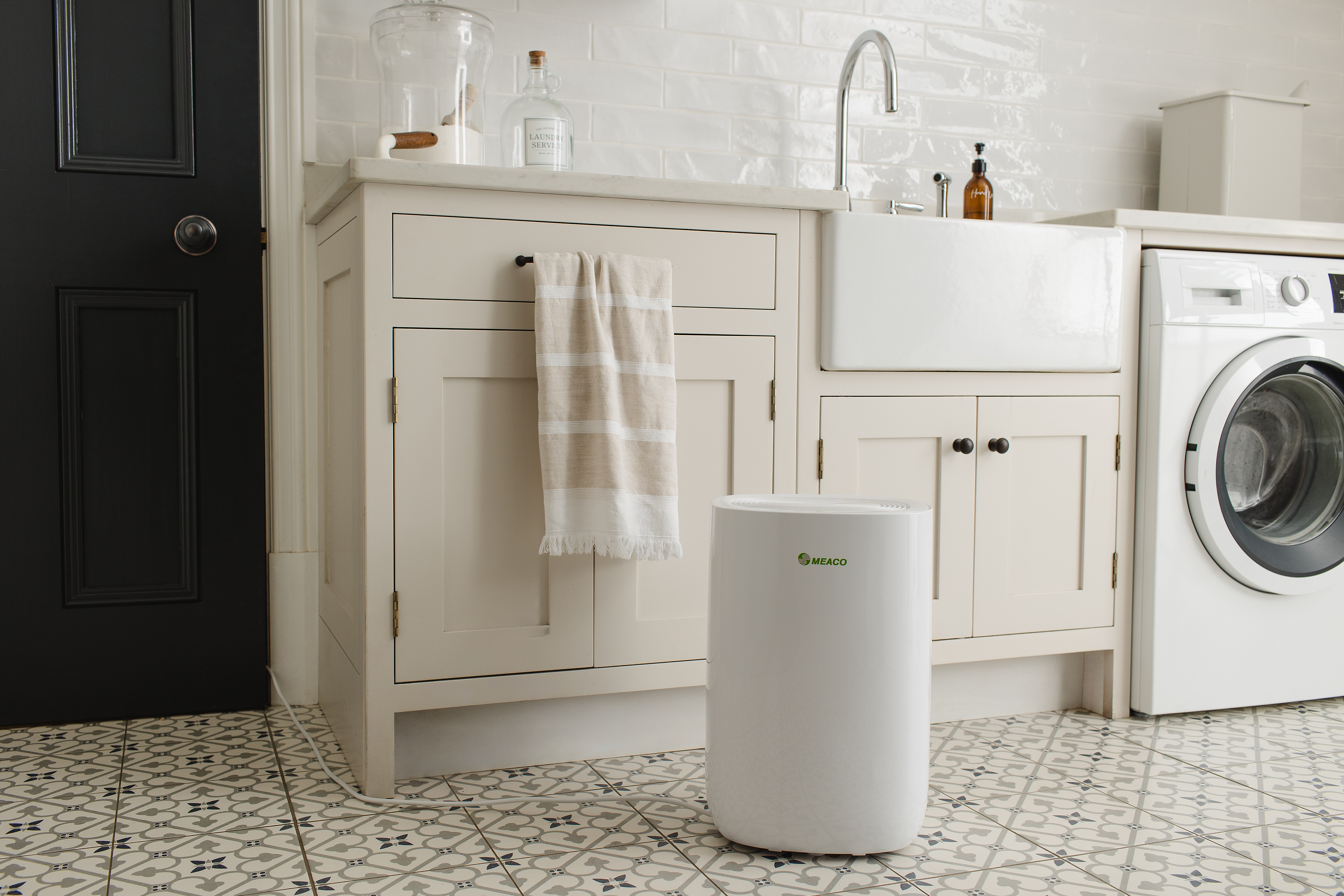 Un deshumidificador blanco se encuentra sobre un suelo estampado junto a una lavadora y un lavabo.