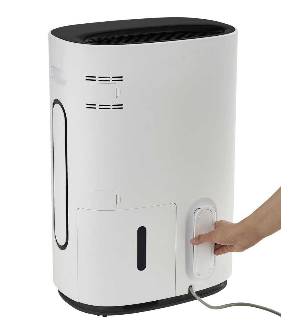 A white dehumidifier with a black top section. A hand operates a white button.