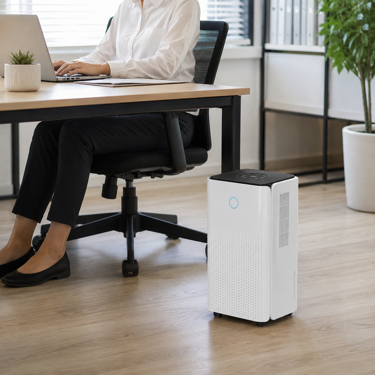 Person working on laptop at desk with white dehumidifier on floor.