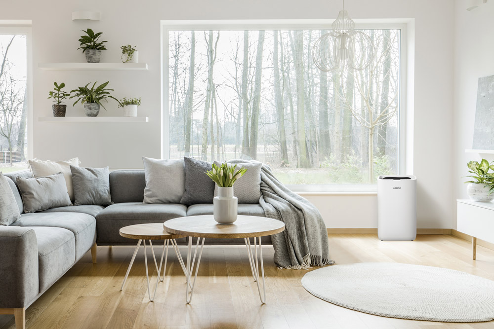 Modern living room with gray sofa, wooden tables, and large window overlooking trees.