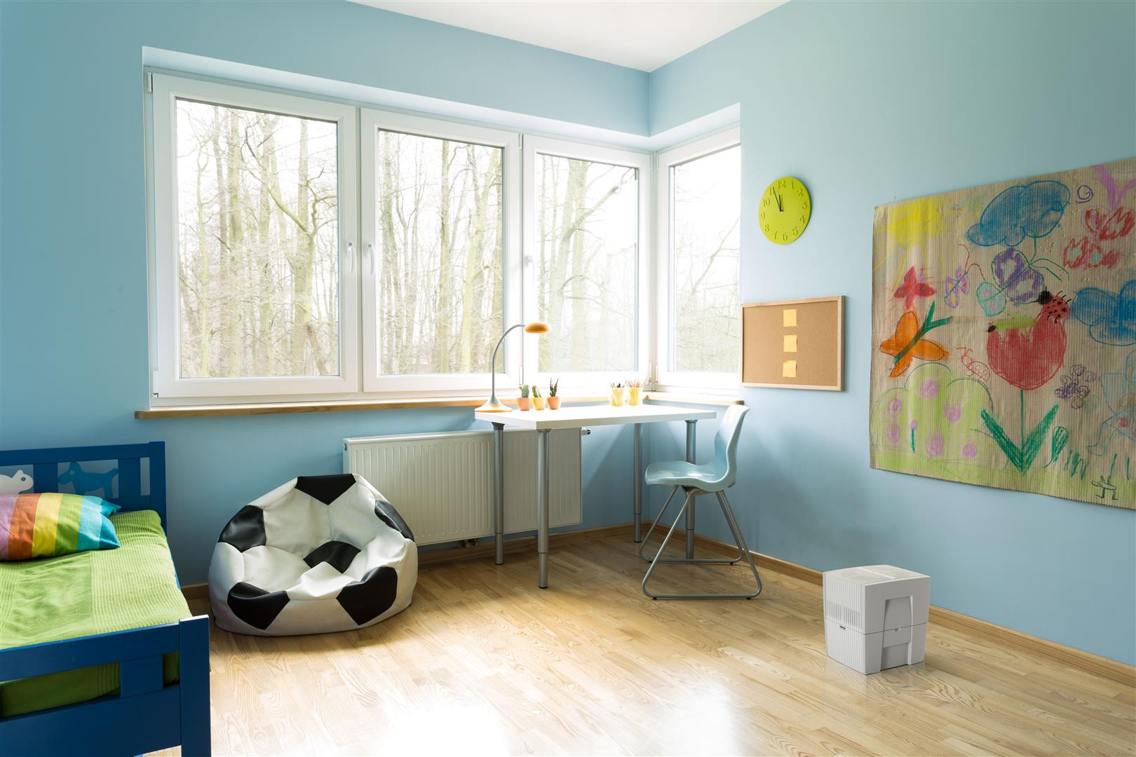 A child's room with a blue bed, soccer beanbag, desk, and colorful wall art.