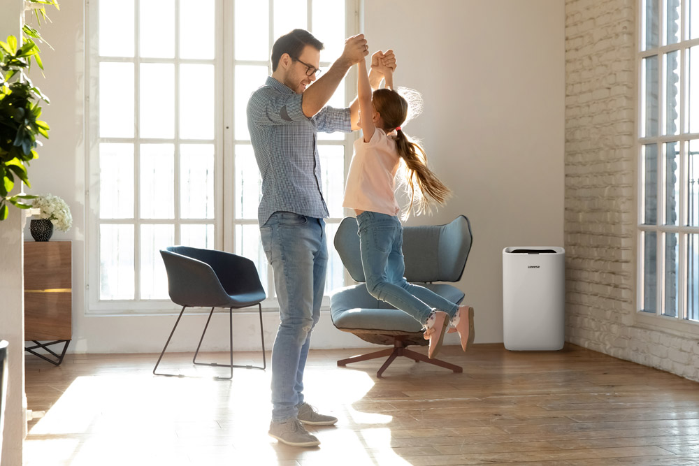 A father lifts his daughter in a living room with an air purifier.
