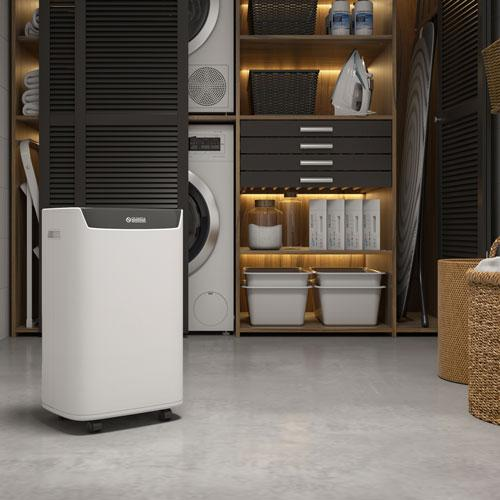 A white dehumidifier stands on a concrete floor next to a washing machine.