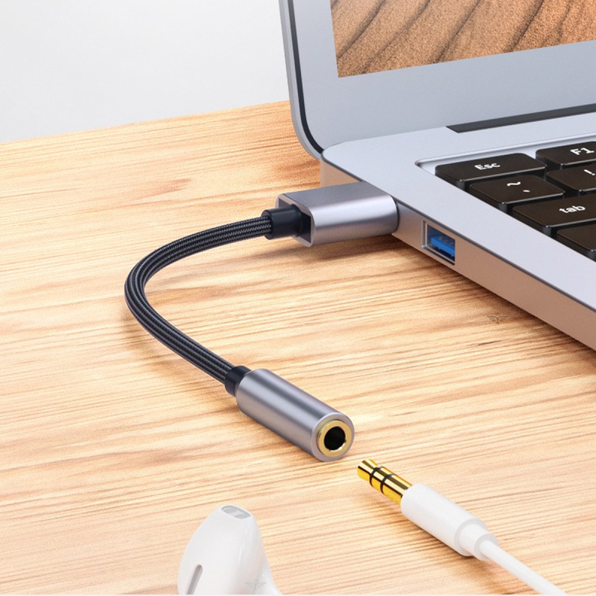 Un cavo adattatore grigio collega un laptop alle cuffie. Una spina dorata è pronta per il collegamento.