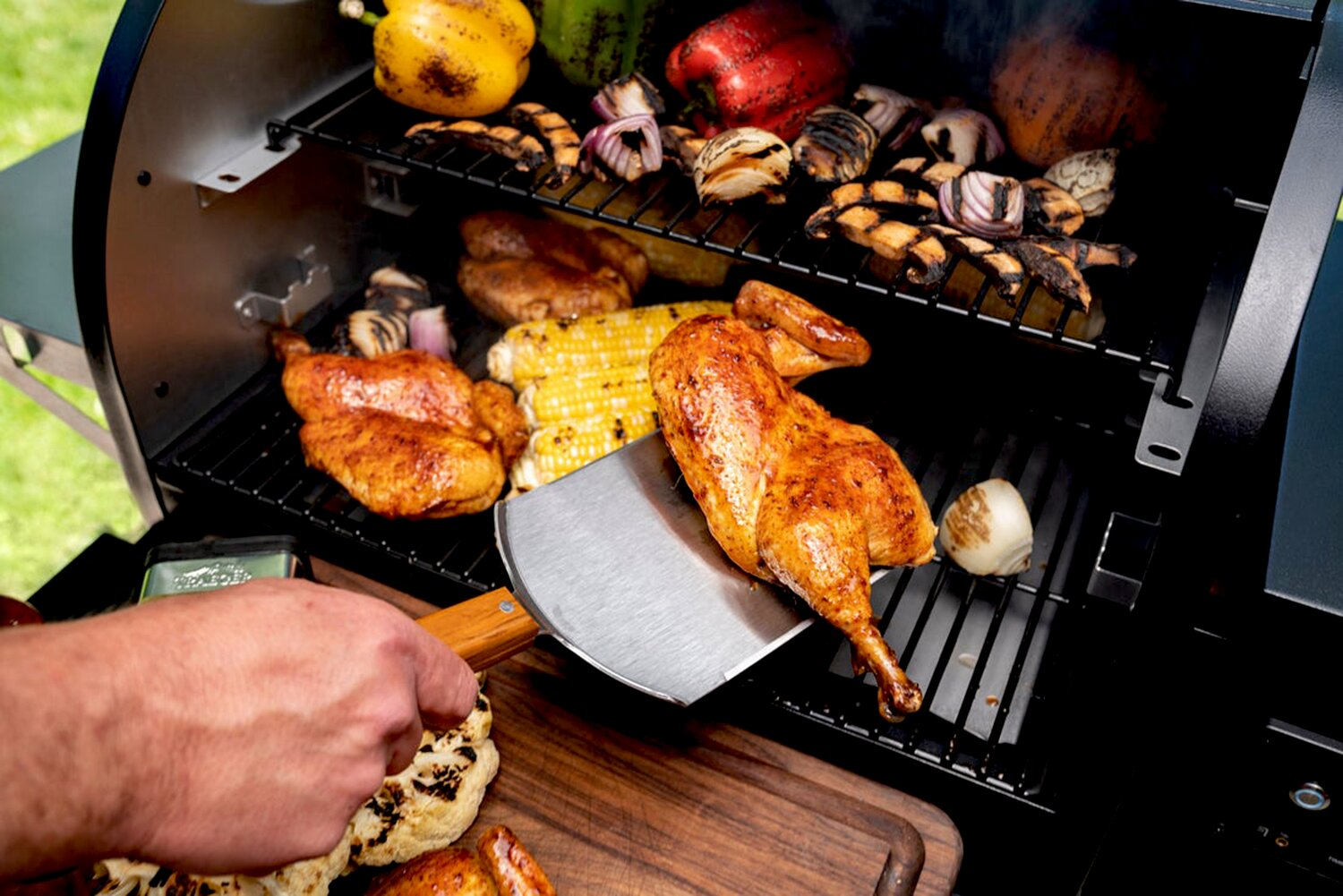 Una persona usa una espátula para voltear un pollo asado dorado en una parrilla.