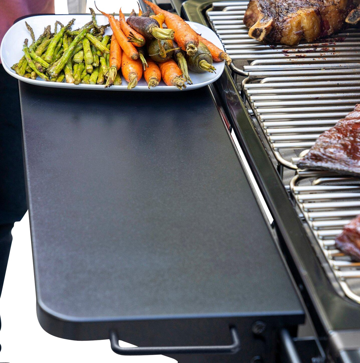 Un plato de espárragos y zanahorias junto a una parrilla con carne.