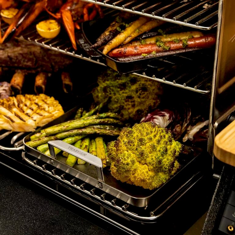 Parrilla con zanahorias asadas, espárragos, coliflor y costillas. Pinzas Traeger en primer plano.