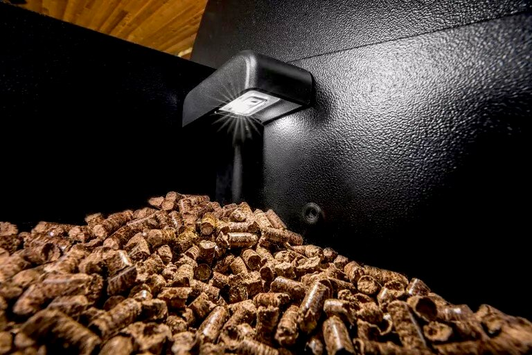 Una pila de pellets de madera frente a una superficie negra texturizada con una luz pequeña.