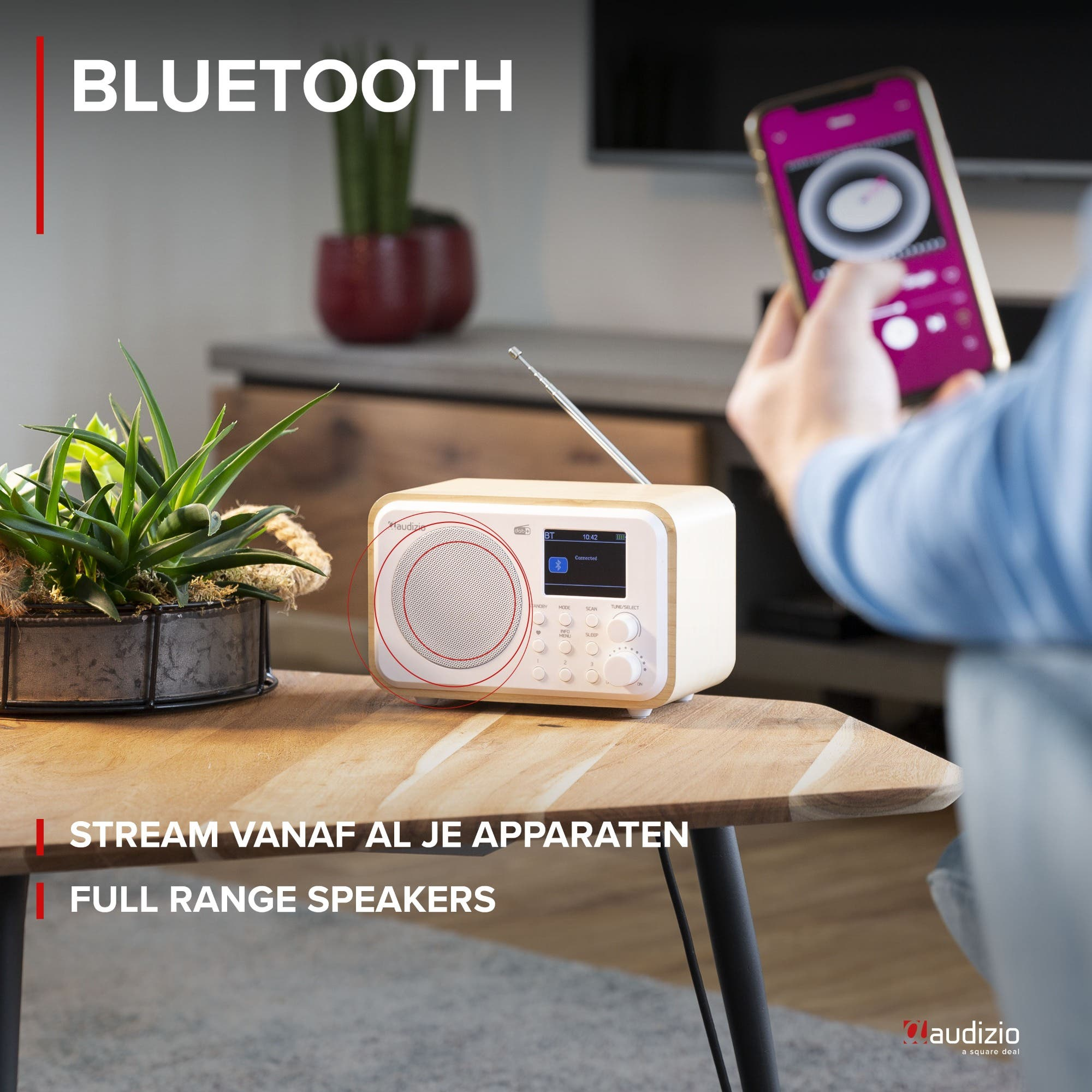 Un altavoz Bluetooth blanco con un teléfono en la mano. Plantas sobre la mesa.