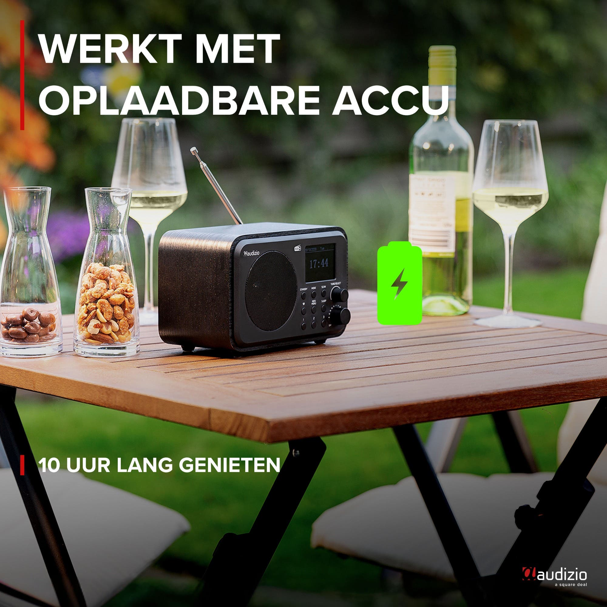 Una radio con batería, vino y aperitivos en una mesa de madera al aire libre.