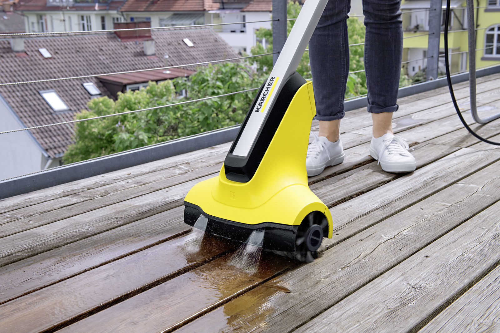 Pulitore Kärcher giallo spazzola un terrazzo in legno con getti d'acqua.