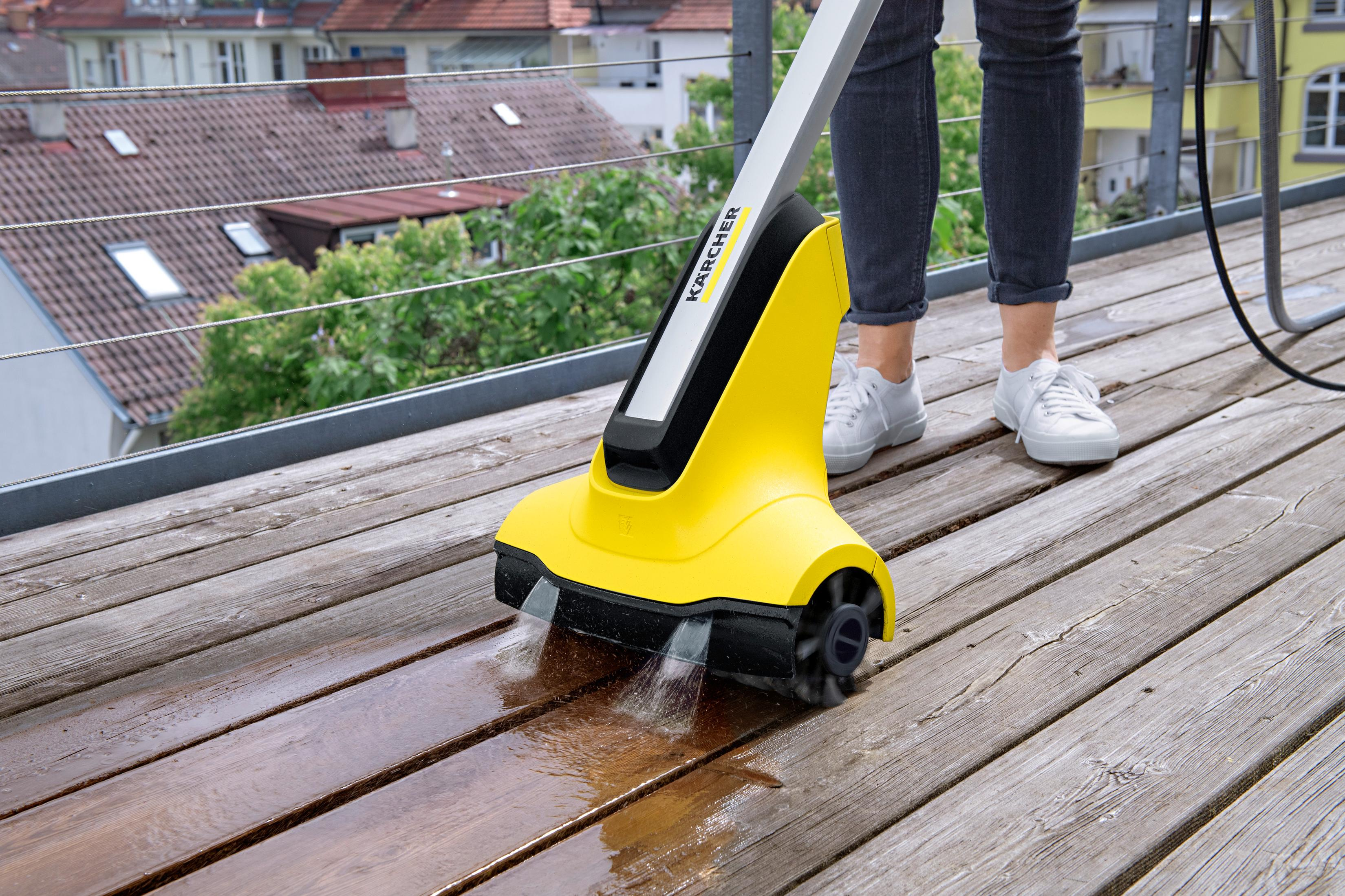 Un pulitore per terrazze Kärcher pulisce un terrazzo in legno con getti d'acqua.