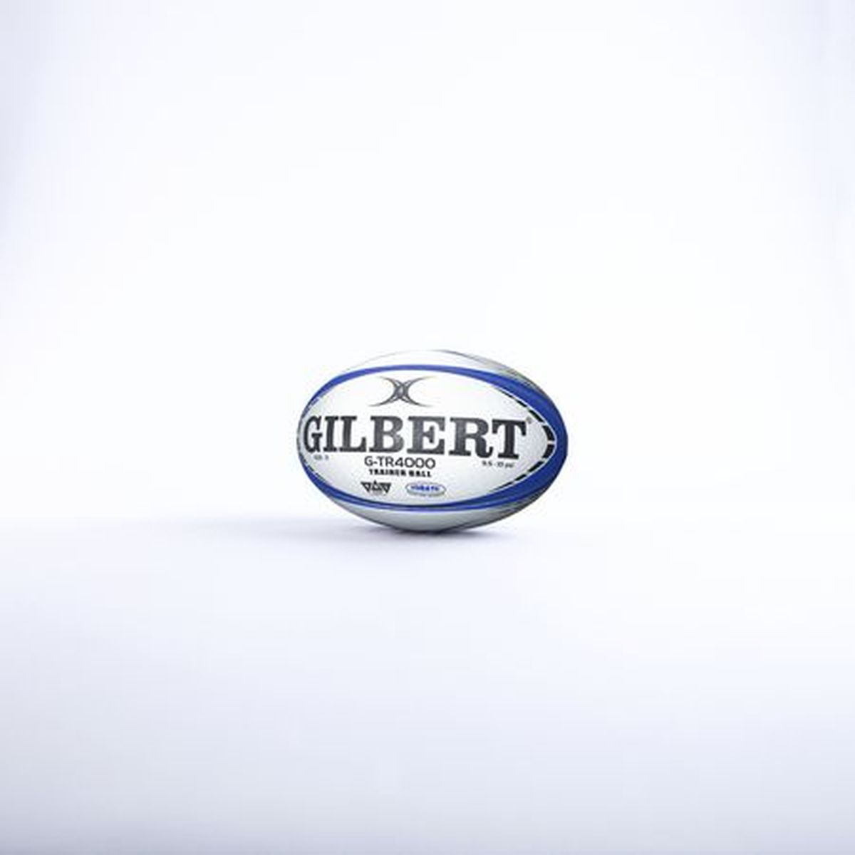 Un pallone da rugby bianco con strisce blu e logo Gilbert poggia su una superficie bianca.