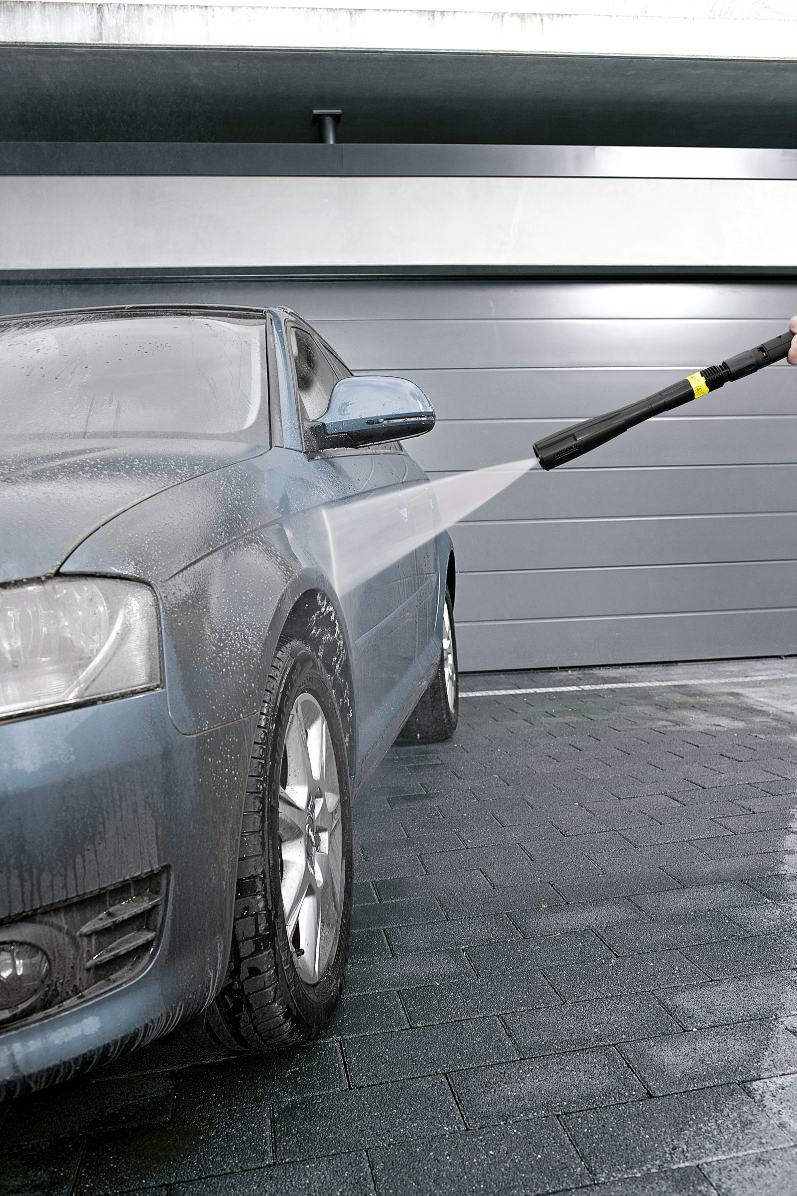 Un'auto blu viene lavata con un'idropulitrice davanti a una porta del garage.