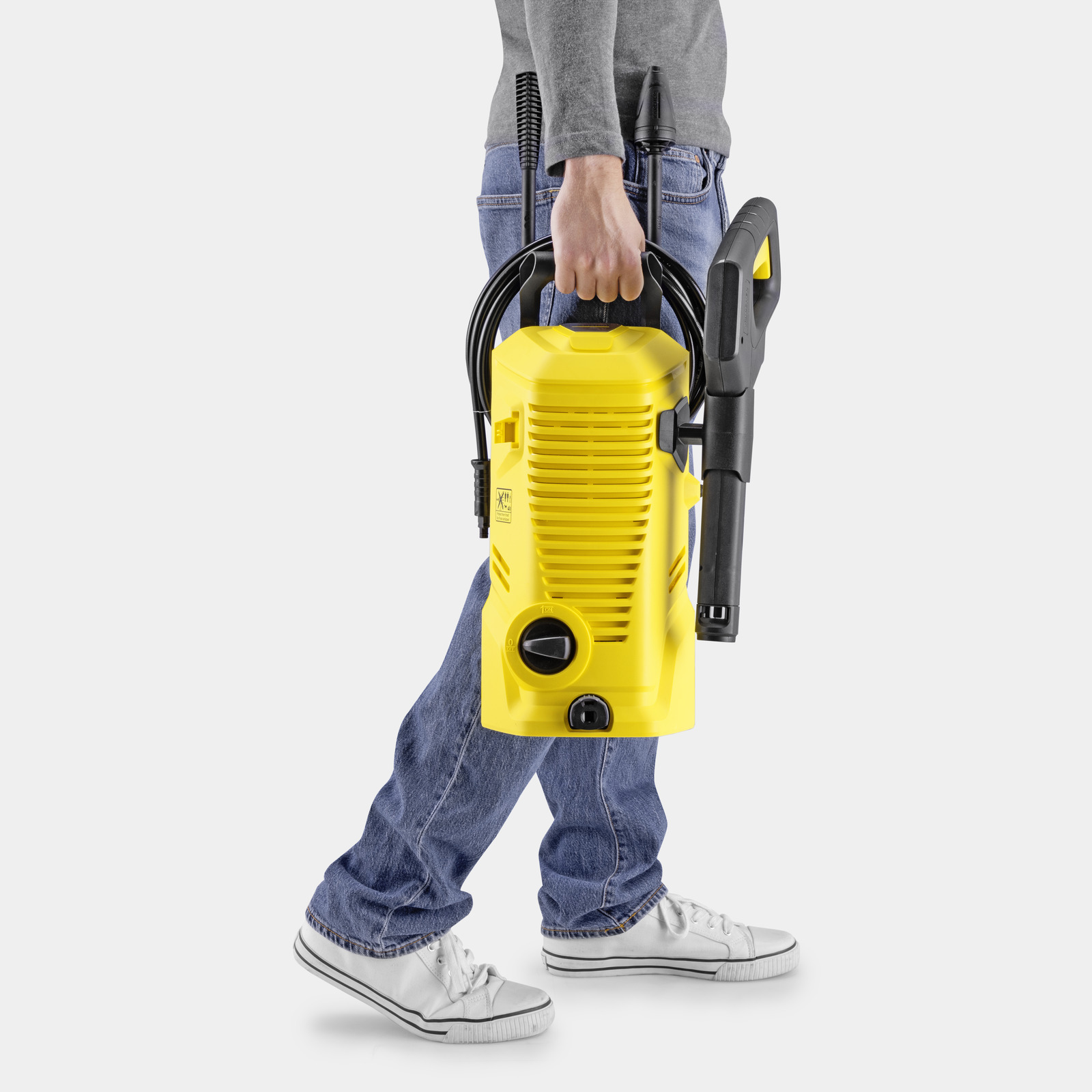 Una persona in jeans porta un'unità idropulitrice gialla con accessori.